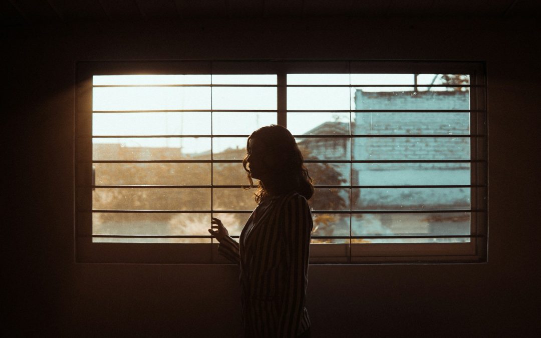 Persona esperando junto a la ventana con el móvil en la mano